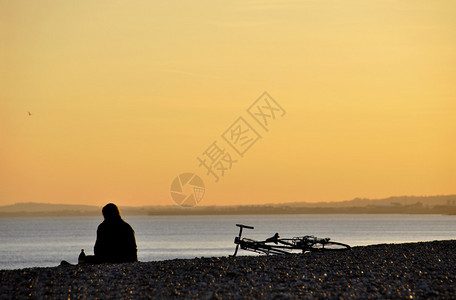 日落时一个坐在沙滩上坐着的人图片