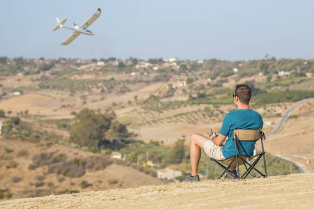 坐在椅子外面玩遥控飞机的年轻男子背面景象图片