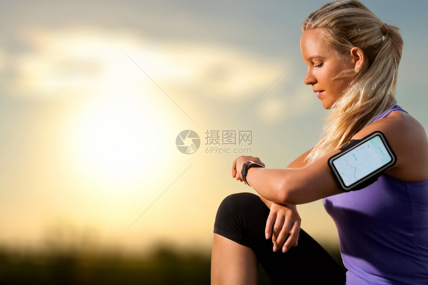 年轻员在日落时在智能手表上检查锻炼的画像戴着智能手表和图形显示锻炼结果图片
