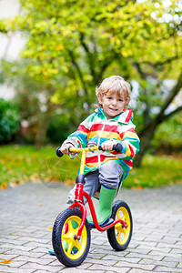 金发美女男孩在雨季夏天或秋天户外骑自行车图片