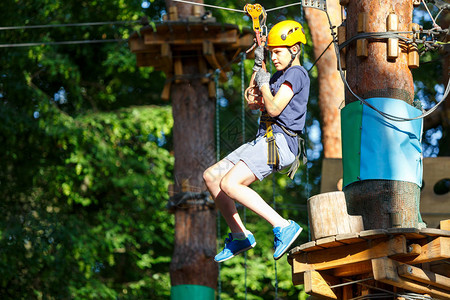 快乐可爱穿蓝T恤和头盔的男孩在冒险公园玩耍玩耍拉绳子爬上木楼梯背景图片