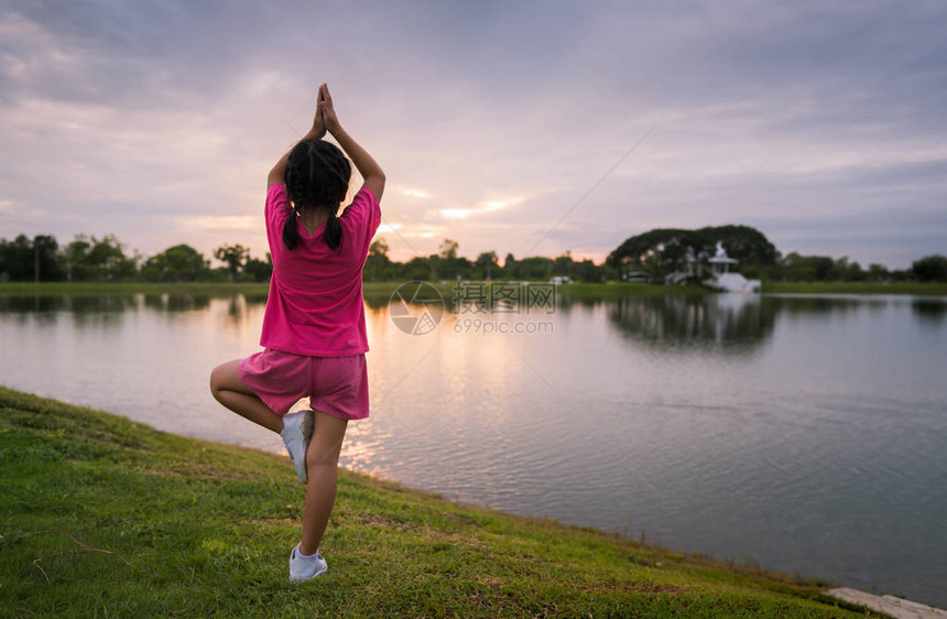 小女孩的背面在公园里做瑜伽或锻炼有日落图片
