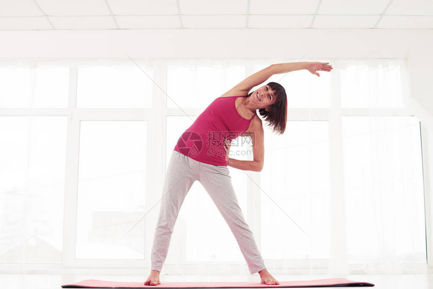 低角度的兴奋的女人站在健身房侧伸展打开位置并诱导平静的感觉站图片