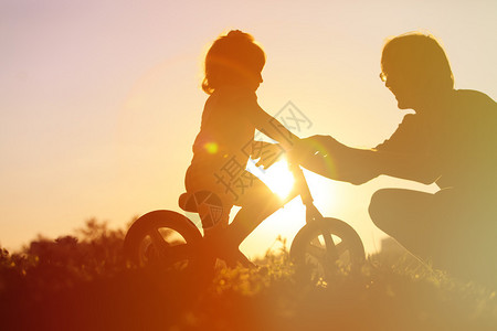 父亲在日落时教女儿骑自行车活图片