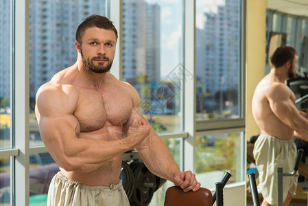 在健身房的健美运动员强壮的男人在健身房锻炼背景上的镜子和运动员在健图片