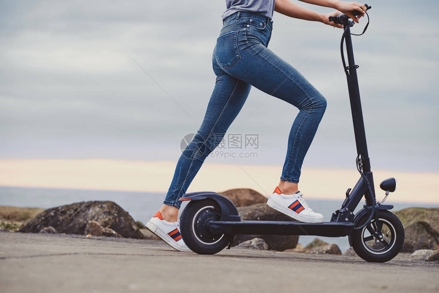 穿着蓝色牛仔裤的感运动女郎正乘着她的新电动摩托车在阴云的图片