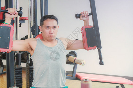 亚洲中年男子在健身房训练手臂设备以图片
