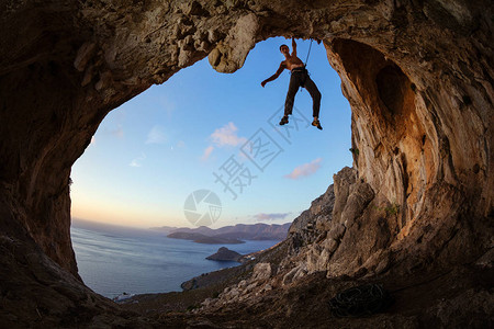 岩石攀岩者紧握在洞穴的天顶上与日落时背景图片