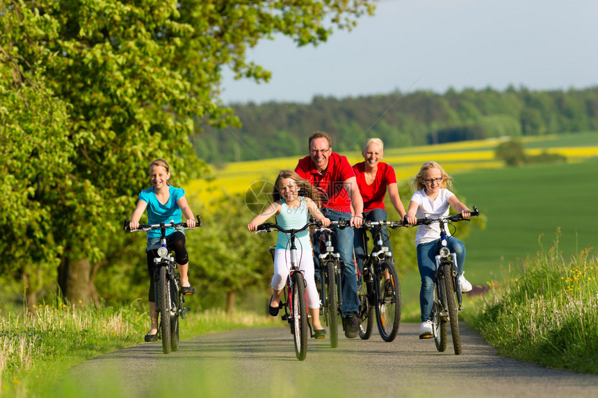 有三个女孩的家庭在美丽的风景中夏日骑自行车或骑自行车图片