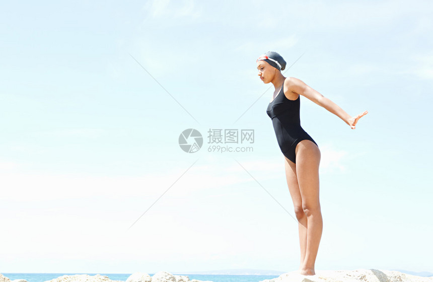 一个美丽的年轻女子游泳潜水员准备从海边的岩石悬崖上跳水图片