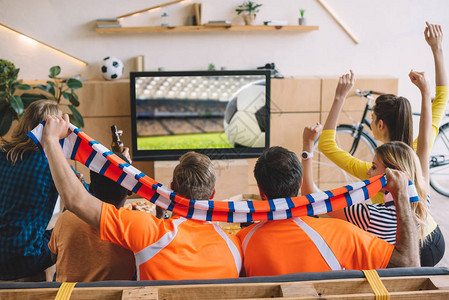 一群足球迷在家里看足球比赛时坐在沙发上庆祝并做是图片