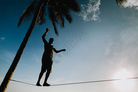 青少年在松弛线上与海滩剪影上的天空景观保持平衡图片