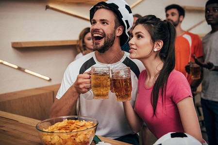 戴着足球帽的兴奋男人和女朋友碰杯啤酒图片