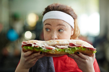 可爱超重女人的近视肖像在她面前拿着大胖子三明治秘密吃着它仔细地环顾四周裹背景图片