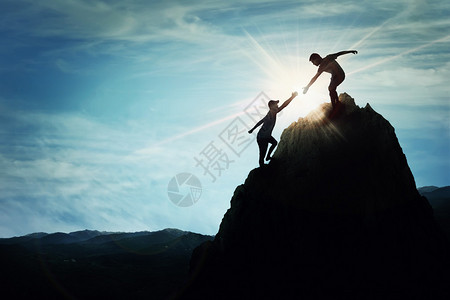 帮助两个男孩攀登一个岩石般危险的悬崖的休战在高山峰上友善的手激励团队信仰和支持符号背景图片