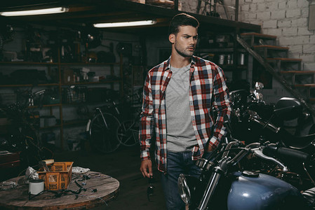 年轻英俊的摩托车手在黑暗修理店里骑图片