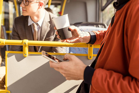 男子在乘坐公共交通工具时使用智能手机持咖啡图片