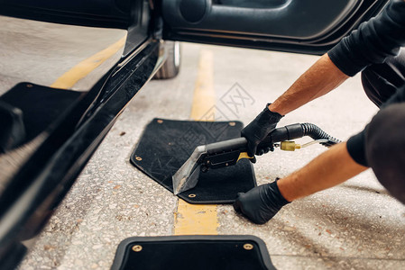 洗车服务男工人戴手套从垫子上除去灰尘和泥土用真空清洁剂对汽车内部图片