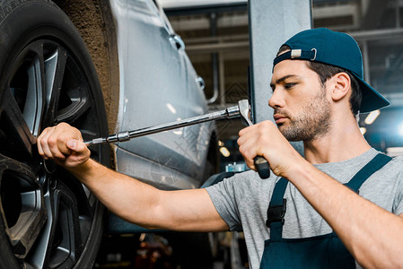 专注于男汽车修理工在汽车修理厂使用车轮扳手图片