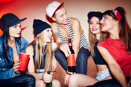 一群朋友享受聚会在私人聚会上坐在沙发上大笑的年轻人在深夜聊天和喝图片