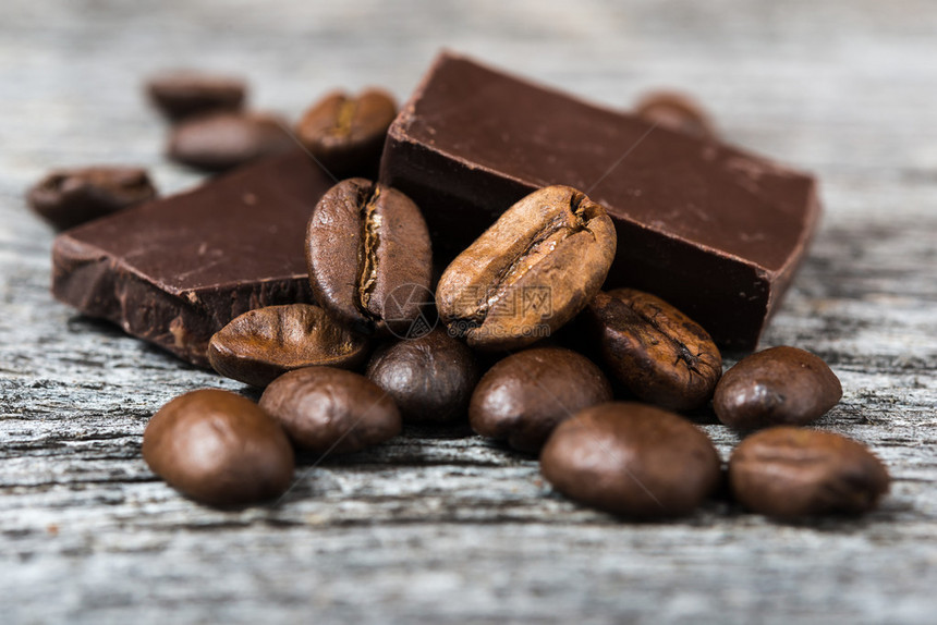 灰色木质背景上咖啡豆和巧克力的特写图片