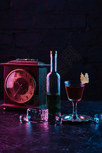 一杯酒精鸡尾酒一瓶酒和深色表面上的古董钟图片