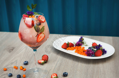 鸡尾酒吧背景含草莓香槟的玫瑰饮料对蓝水管的冰和新鲜浆果配制饮料食图片