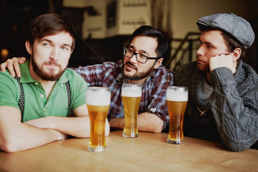 三个男人坐在桌子上拿着高的杯子盛着新鲜酿造的白发啤酒享图片