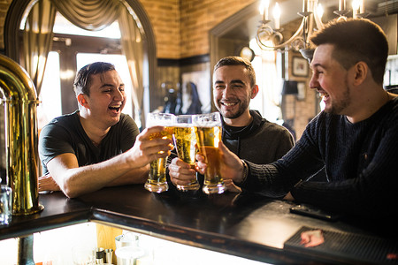 三个快乐的年轻男子在坐酒吧柜台共坐时图片