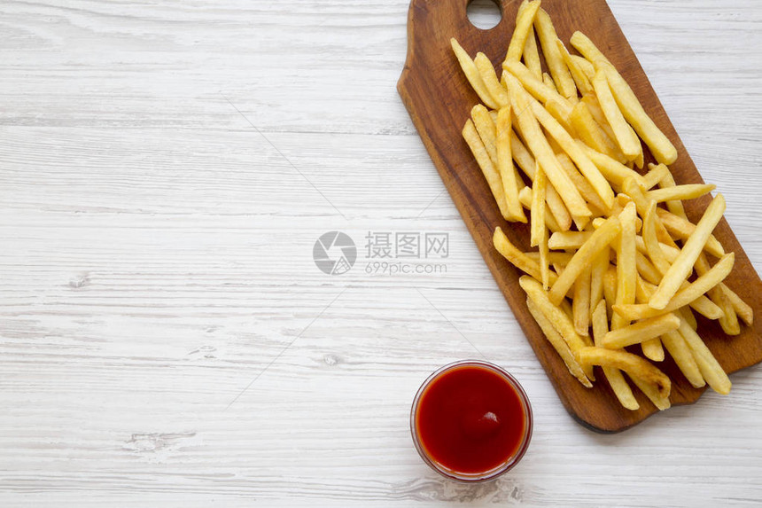 木板上的炸薯条和白色木制背景的番茄酱图片