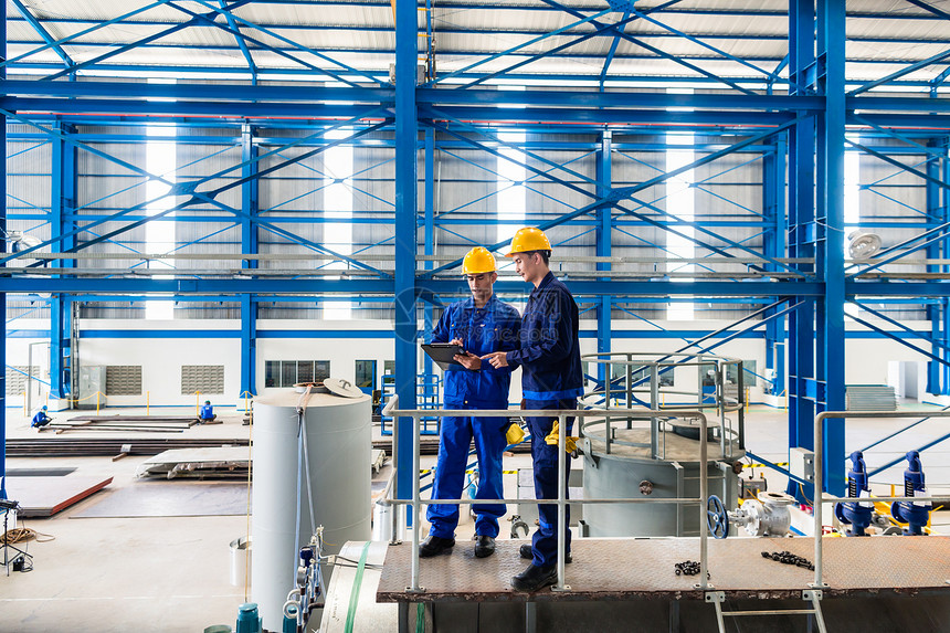 两名工人在大型金属车间或工厂检查工作时站在大型图片