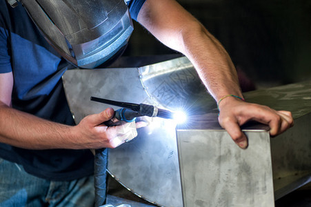 金属工匠在一个车间中用工业焊接器焊接两个金属部件图片