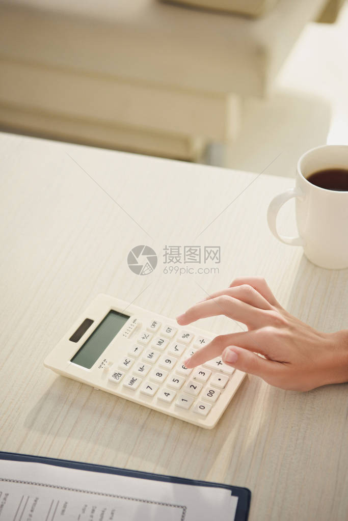 妇女依靠咖啡杯子桌上的计算器进行经济核算图片