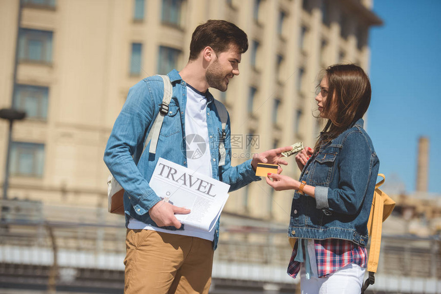 拿着旅行报纸的男游客拿着信用卡给女图片