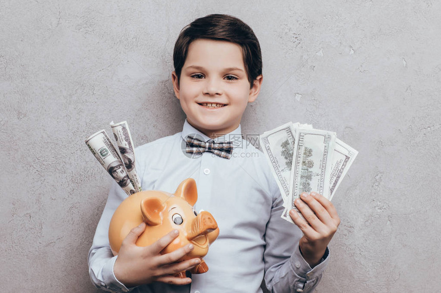 微笑的小男孩的肖像拿着小猪银行和图片