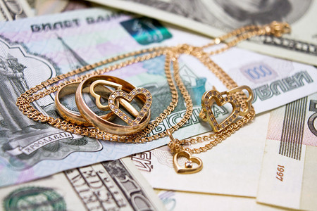结婚戒指金链子和心形耳环躺在钱上图片