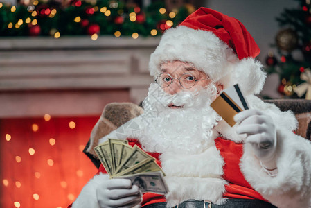持有信用卡和美元钞票的传统红装扮中的Santa背景图片