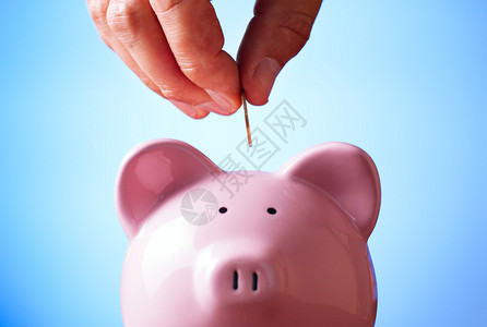 在储蓄和投资概念中将一枚硬币放进小猪银行的空位里的图片