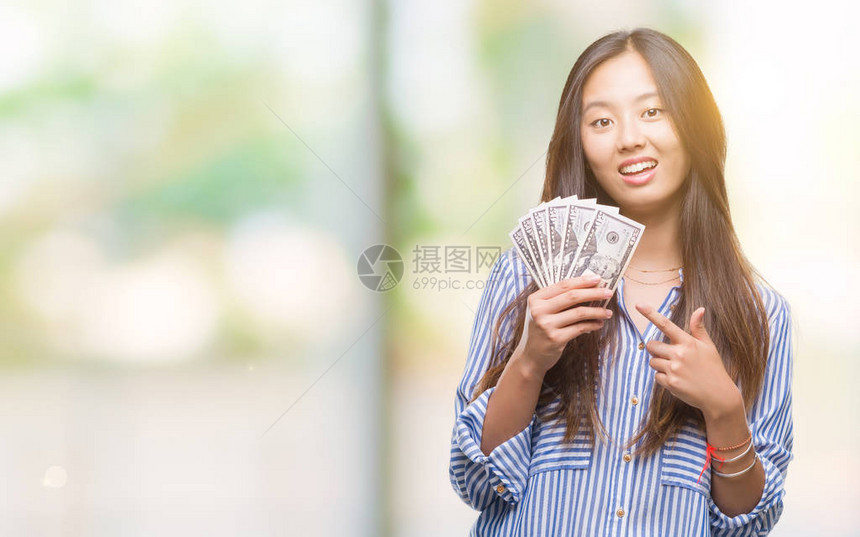 年轻的亚洲女在孤立的背景中持有美元非常快乐地用手和指图片