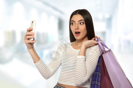 带着彩色袋子购物的年轻美丽快乐女孩在移动相机上拍到自己的照图片