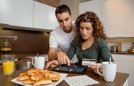年轻夫妇的肖像与电子平板电脑审查信用卡每月支出图片