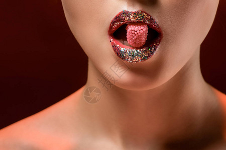 有闪亮嘴唇的年轻女子将粉红色糖果握在布贡图片