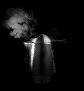 黑色背景下的蒸汽和银色茶壶中的沸水图片