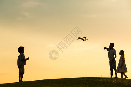 日落时三个孩子正在玩飞机玩具图片