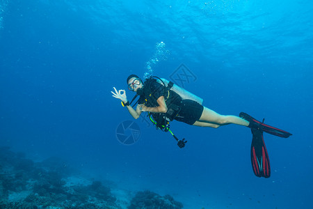 探索海底的年轻女子水肺潜水员显示好的迹象与美丽的岩石和珊图片