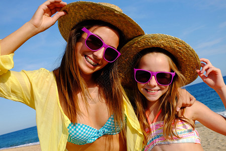 在海滩上穿着草帽和有趣的紫色墨镜的年轻妈和女儿近距离露天肖像背景图片