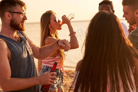 热闹而兴奋的年轻朋友一边在海滩派对上玩乐一边喝甜菜图片