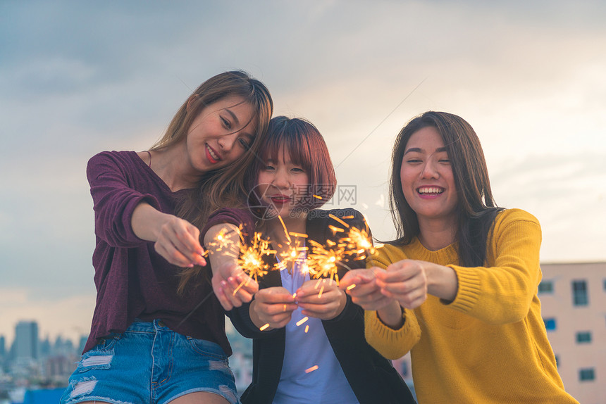 年轻人在屋顶派对上的户外拍摄一群快乐的亚洲女孩朋友在傍晚日落时分在屋顶派对上享受和玩烟火节日庆祝节日派对青少年图片