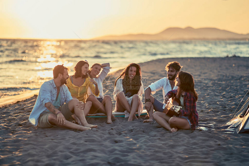 一群带着吉他在海滩上微笑的朋友朋友们在沙滩上用吉他和唱歌图片