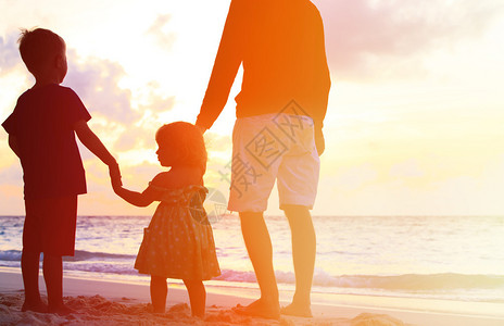 日落时父亲和两个孩子在海滩图片